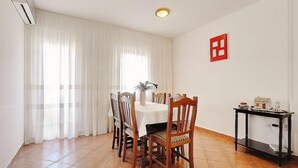 Un coin repas avec une table dressée pour quatre personnes, entourée de chaises en bois. On y trouve une petite table d’appoint sur laquelle sont posés une maquette de maison et un vase.