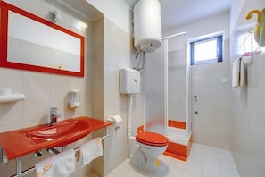 Et badeværelse med en rød vask, et hvidt toilet og et bruseområde.