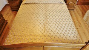 Una cama de madera con una colcha estampada, dos mesitas de noche con lámparas y un cabecero de madera.