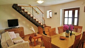 Una sala de estar con sofá, mesa de centro, mesa de comedor con sillas, televisor, escalera y puerta.
