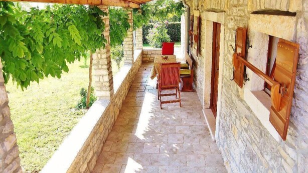 Edificio de piedra con una pérgola de madera, un banco de piedra y vistas al verdor.