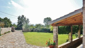 Un sendero de piedra conduce a un patio cubierto con un muro de piedra y un jardín con césped.