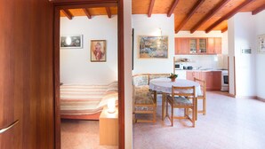 A cozy room with a bed, a bench, and a dining table with chairs. There is a kitchen area with cabinets and appliances. - Apartment Nada / One Bedroom (Rovinj)