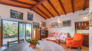 A cozy living room with a wooden ceiling, a floral sofa, a bright orange armchair, and a table with a crocheted tablecloth. - Apartment Nada / One Bedroom (Rovinj)