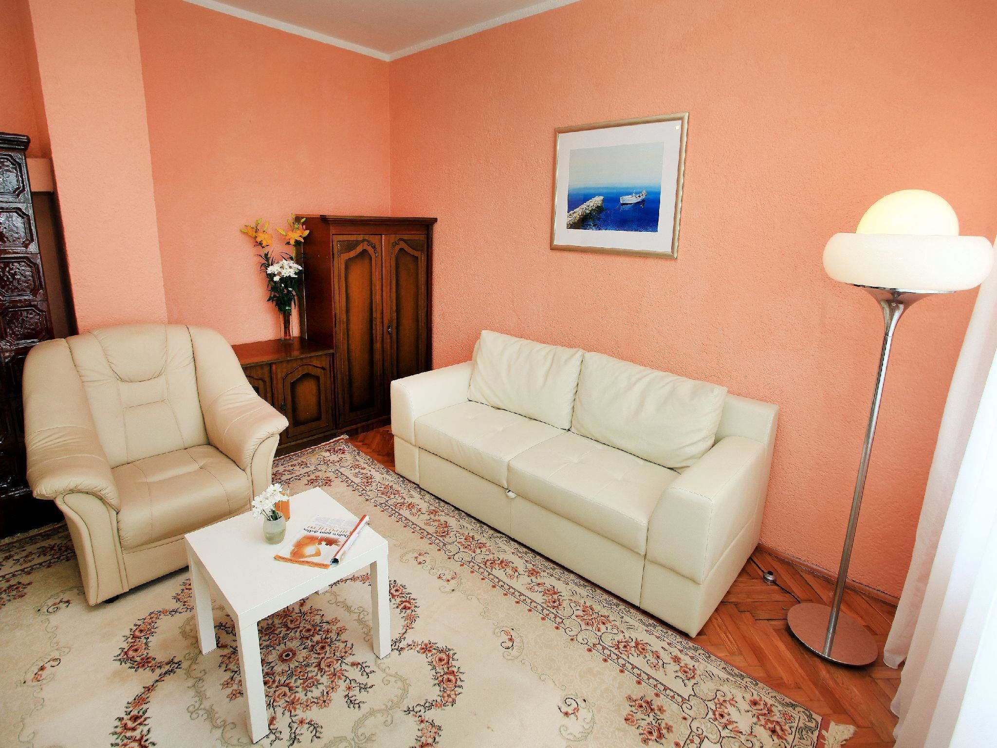 A living room with a beige armchair, a white sofa, a small white table, a wooden cabinet, a framed picture on the wall, and a floor lamp.