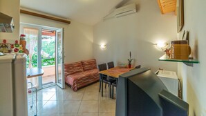 A compact living space with a sofa, dining table, and chairs, a refrigerator, and an air conditioning unit. - Apartment Andrea / Galery one Bedroom (Vodnjan)