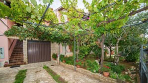 A stone-paved courtyard with a wooden staircase leading to a brown gate, surrounded by potted plants and a pergola with climbing vines. - Apartment Andrea / Galery one Bedroom (Vodnjan)