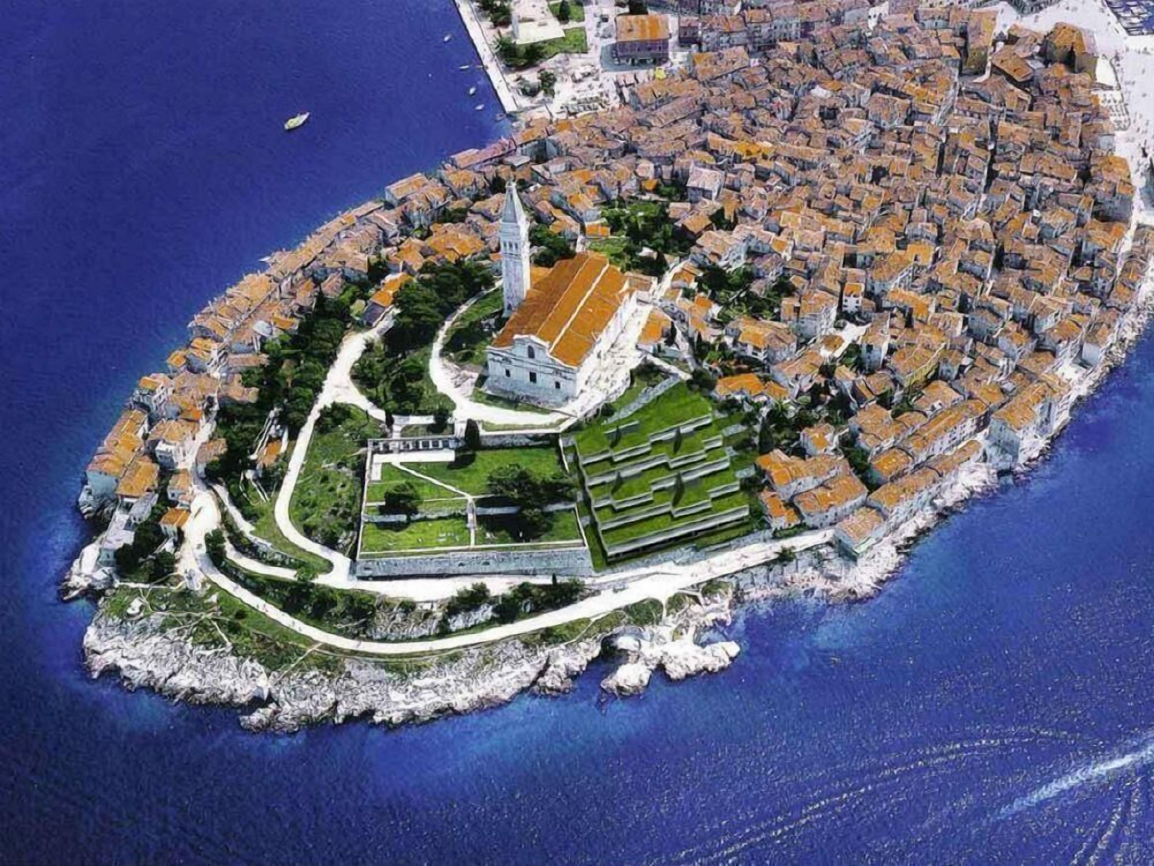An aerial view of a coastal town with a fortified structure, narrow streets, and a prominent tower.