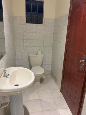 A small bathroom with a toilet, sink, and a window above the toilet. - Wasafi Garden & Spa Kibiko (Nairobi)