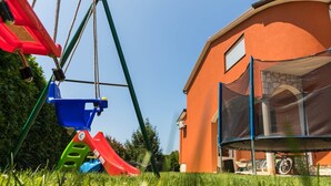 A swing set with a red slide and a blue bucket, a trampoline with a safety net, and a house with an orange exterior and a stone facade. - Apartments Ana Pula / Exclusive two Bedroom A5 (Pula)
