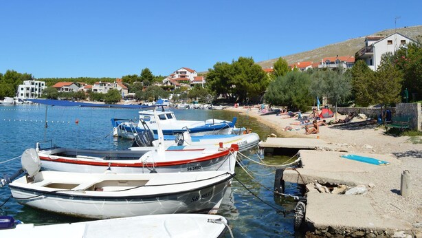 A marina with boats docked, a sandy beach, and houses in the background.