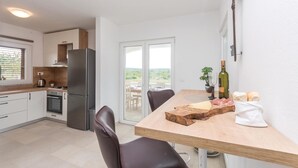 Uma cozinha moderna com geladeira embutida, uma mesa de jantar com cadeiras e vista para área externa por uma porta de vidro.