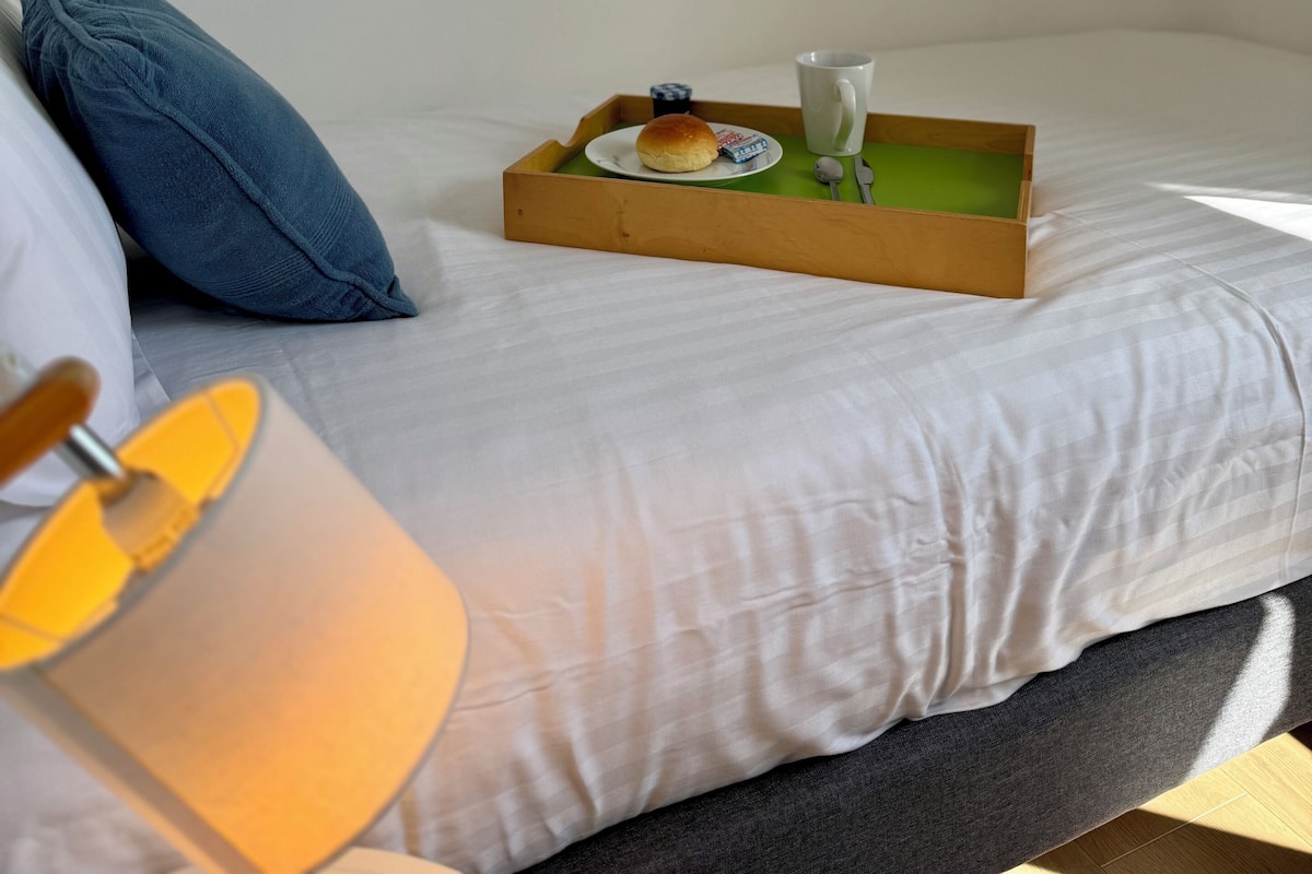 A neatly made bed with a tray of breakfast items, a lamp, and a butterfly wall decoration.