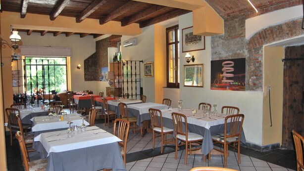 A restaurant with multiple tables and chairs, wooden beams on the ceiling, and framed pictures on the walls. - Ristorante Albergo Arcade (Grandate)