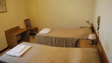 A hotel room with two single beds, a wooden desk, a chair, and a bedside table with a lamp.
