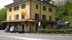 A two-story building with a yellow facade, a sign indicating it is an arcade, and a covered entrance with a car parked in front. - Ristorante Albergo Arcade (Grandate)