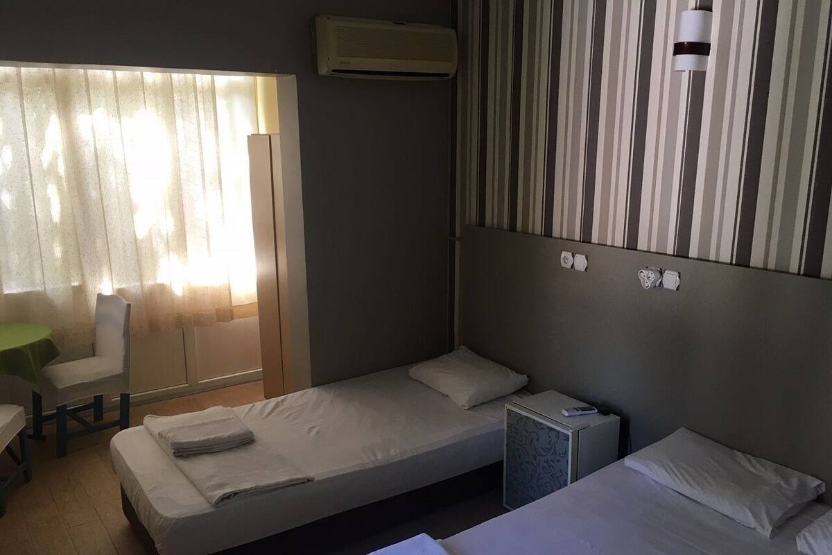 A hotel room with two single beds, a small desk with a chair, a window with curtains, and a striped wall design.
