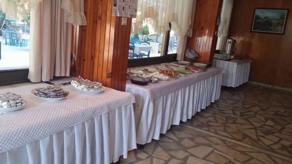 Montaje de bufé con diversos alimentos sobre mesas blancas, paredes de madera y un suelo con diseño.