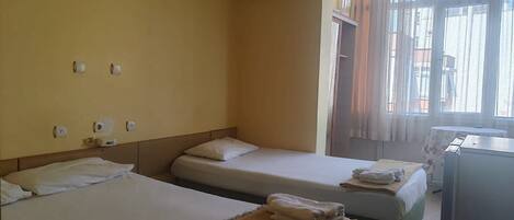 A hotel room with two single beds, a small desk, a window with curtains, and an air conditioning unit on the wall.