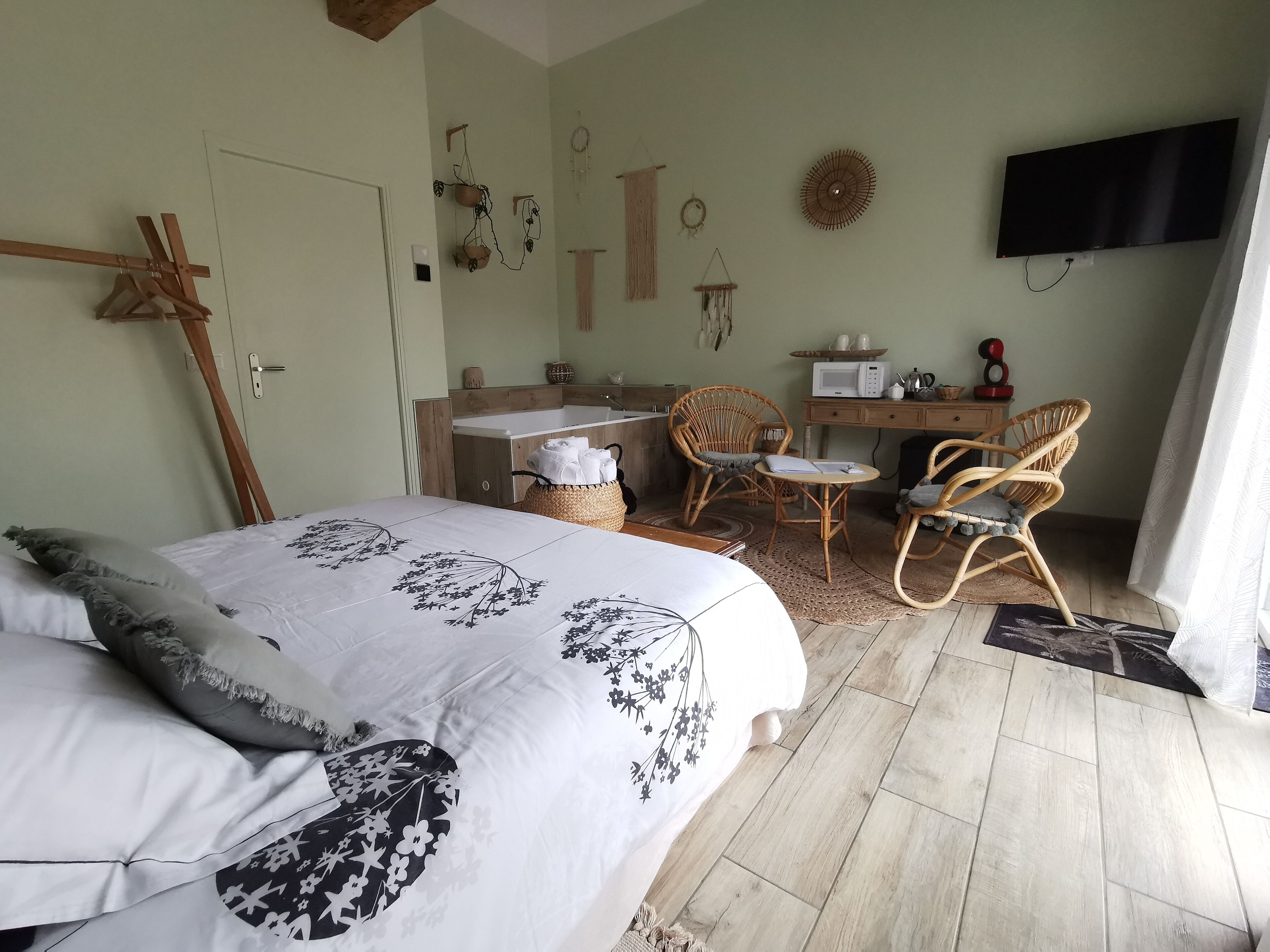 Un dormitorio con una cama, dos sillas de mimbre, un escritorio con un microondas y un televisor montado en la pared.
