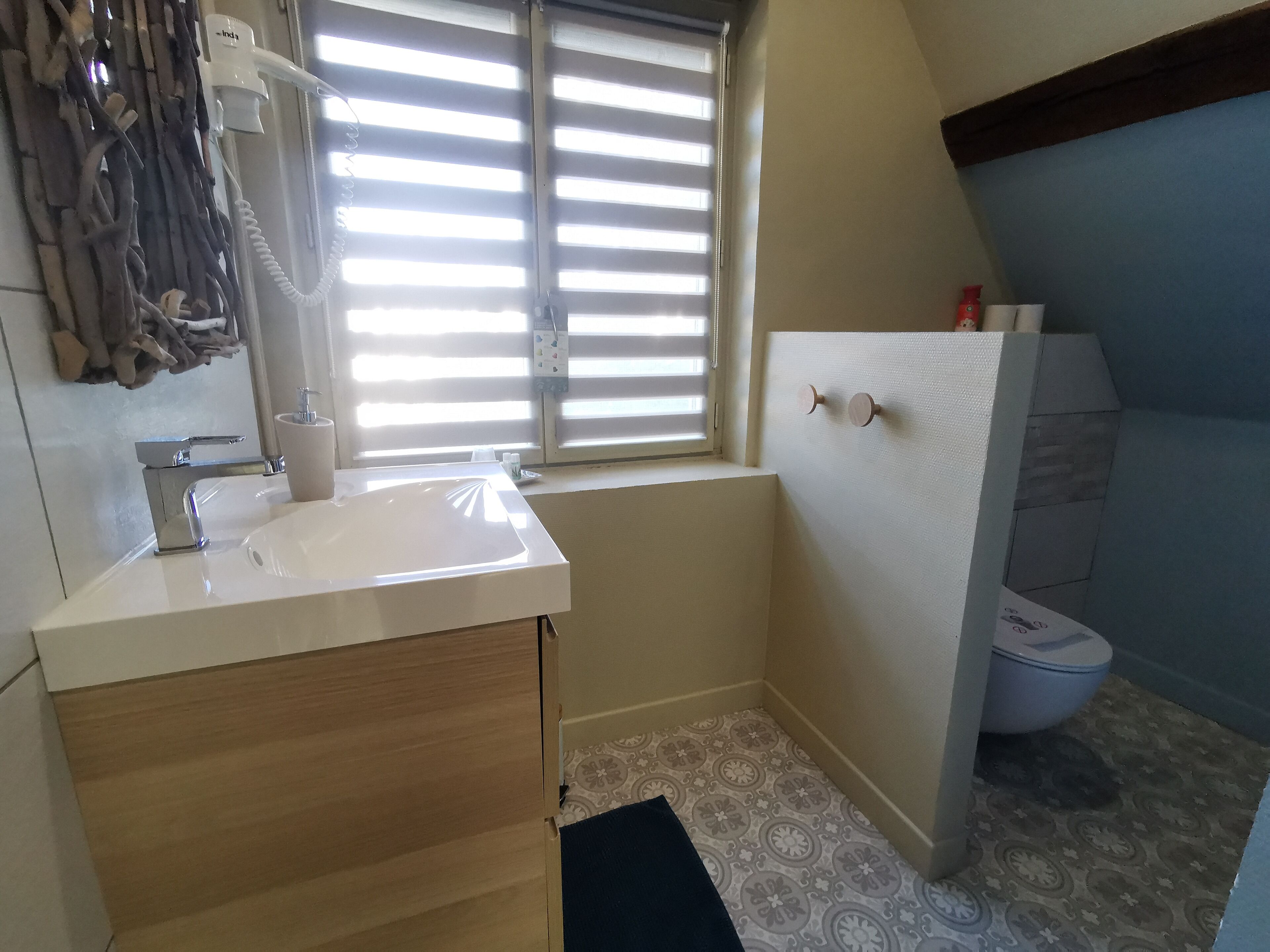Un baño pequeño con lavamanos, inodoro y ventana con persianas.
