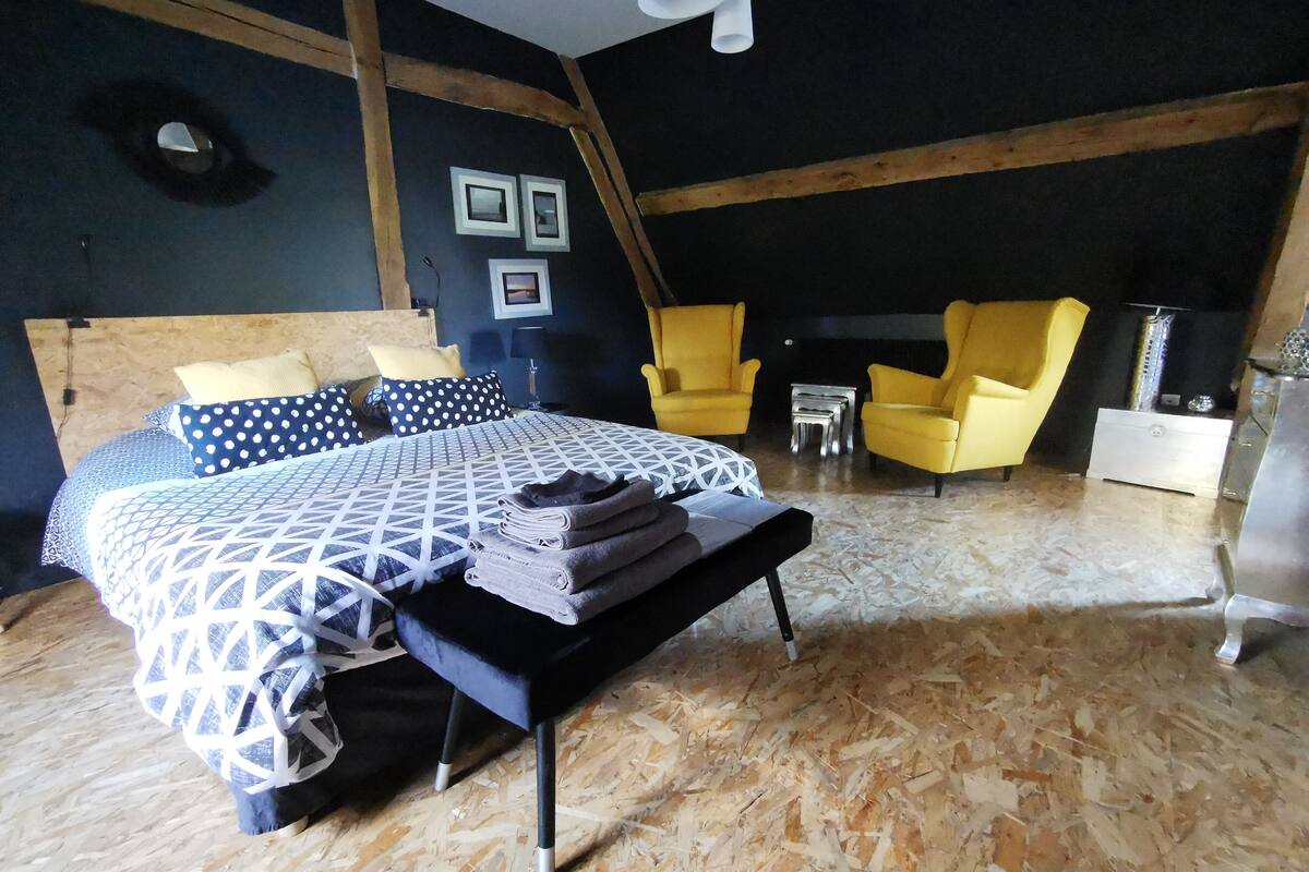 A bedroom with a bed, two chairs, a small table, and a dresser.