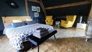 A bedroom with a bed, two chairs, a small table, and a dresser.