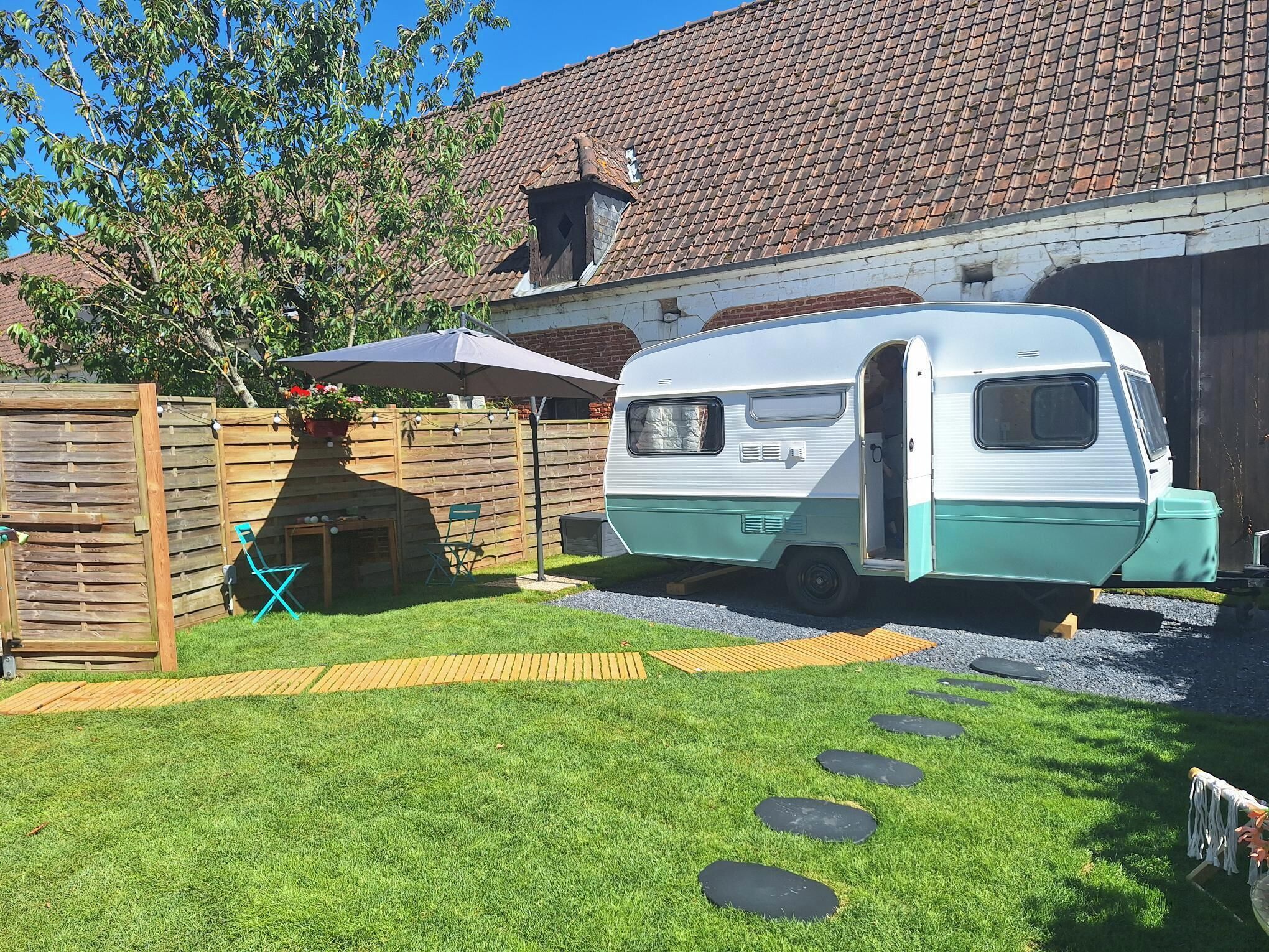 Une caravane était garée dans une cour arrière, avec un toit recouvert de tuiles, une clôture en bois et une pelouse verdoyante parsemée de pierres plates servant de pas.