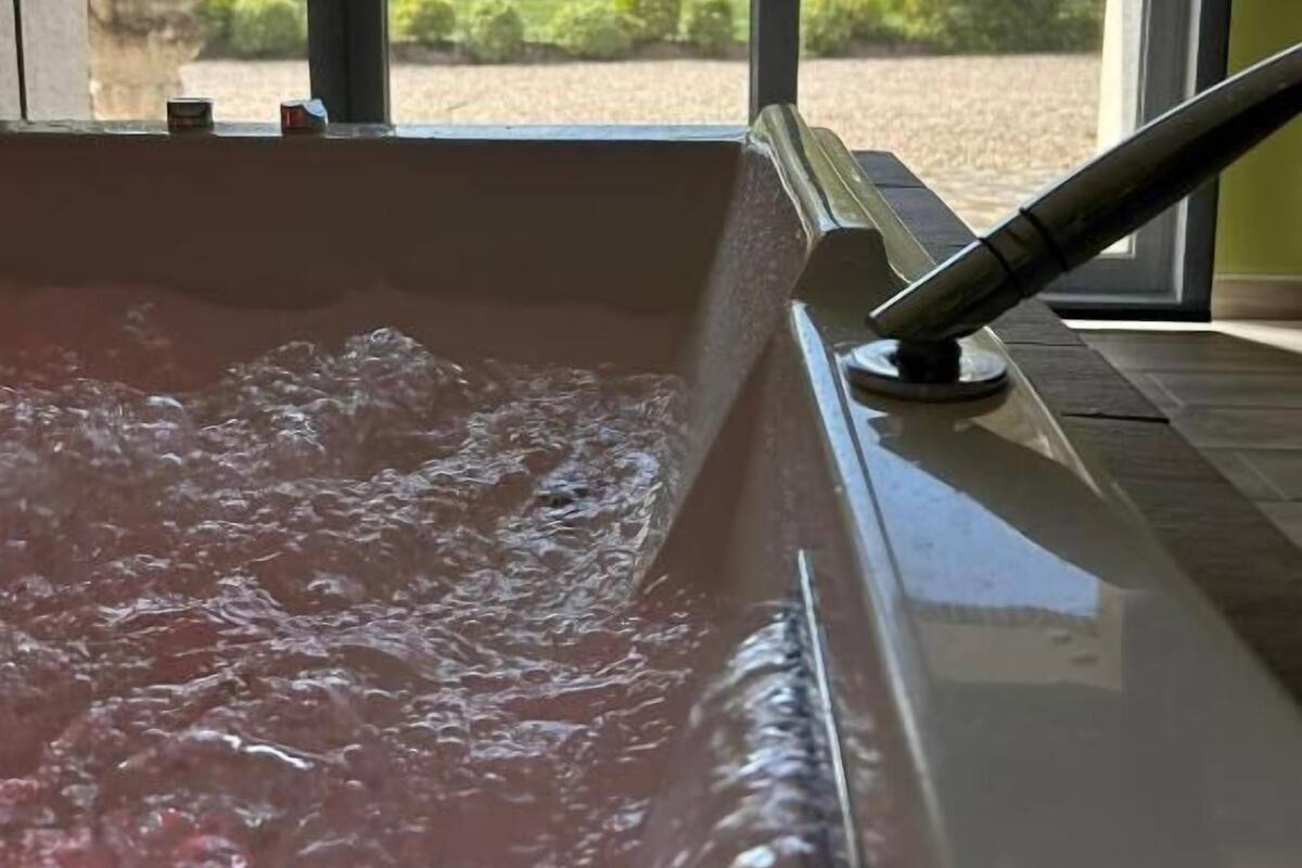A hot tub with a view of a building and trees through large windows.