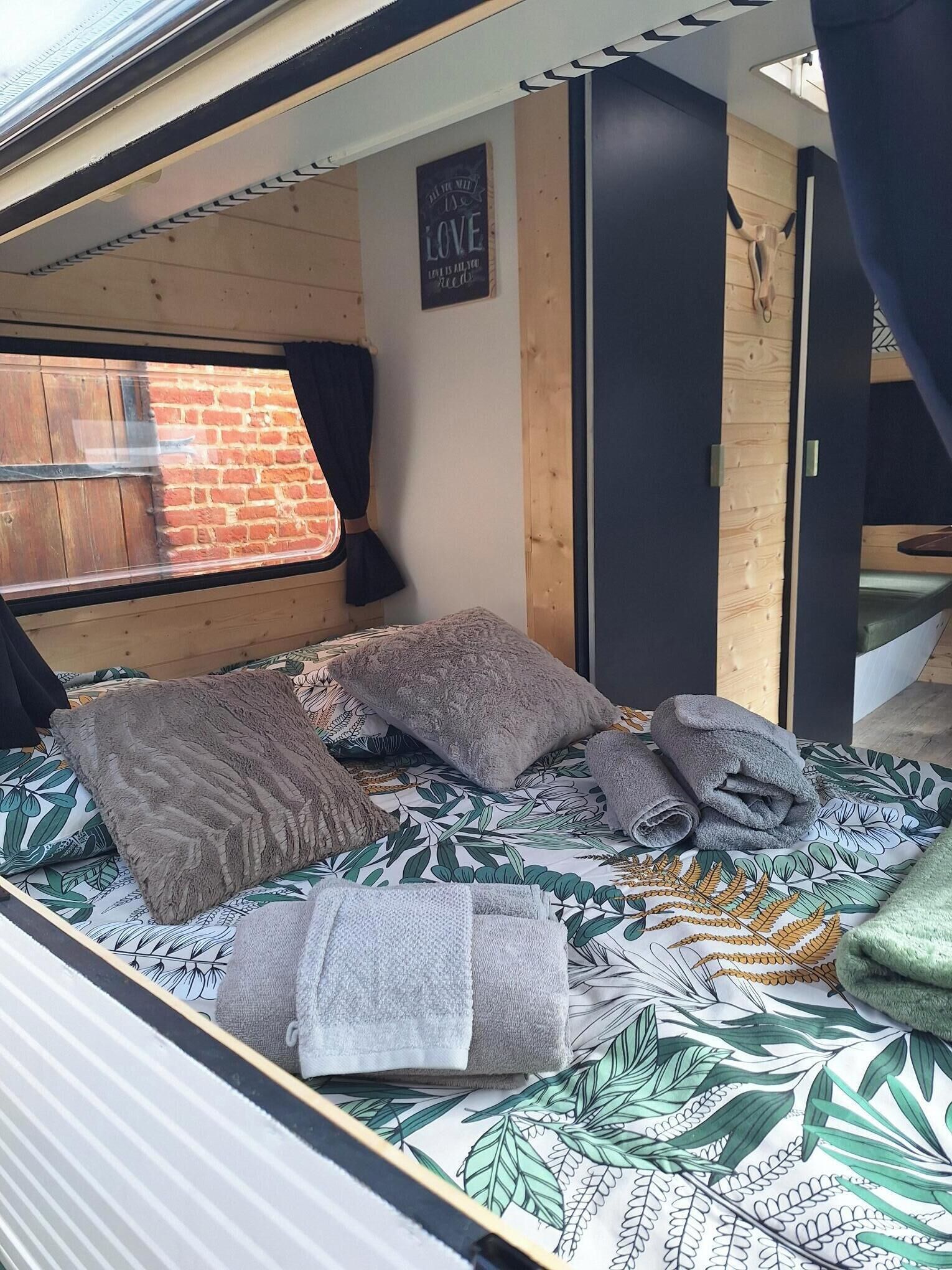 A cozy RV bedroom with a bed, pillows, and a window with curtains.