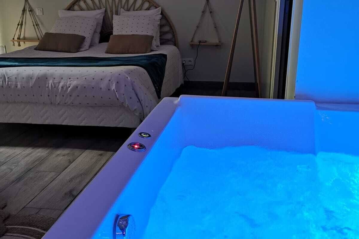 A bedroom with a bed, a wooden floor, and a hot tub with blue lighting.