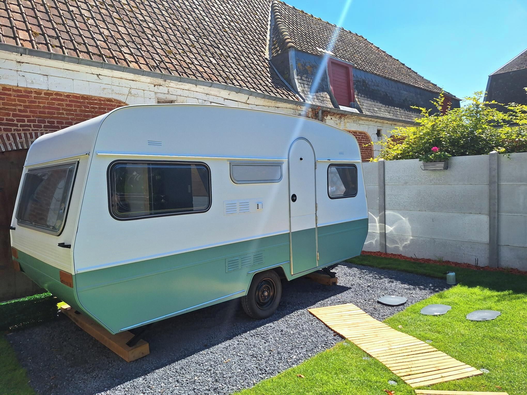 A vintage camper parked in a driveway with a house in the background.