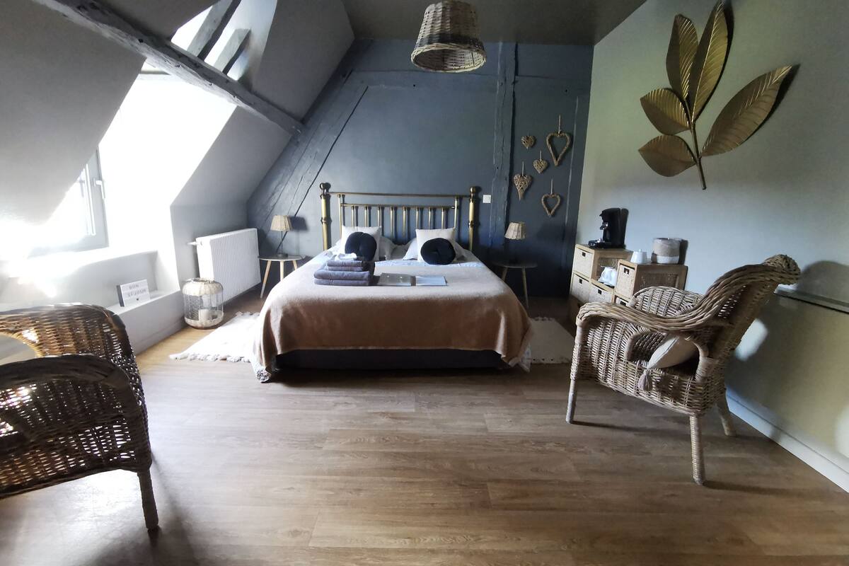 A bedroom with a bed, two wicker chairs, a small table, and a wall-mounted shelf.
