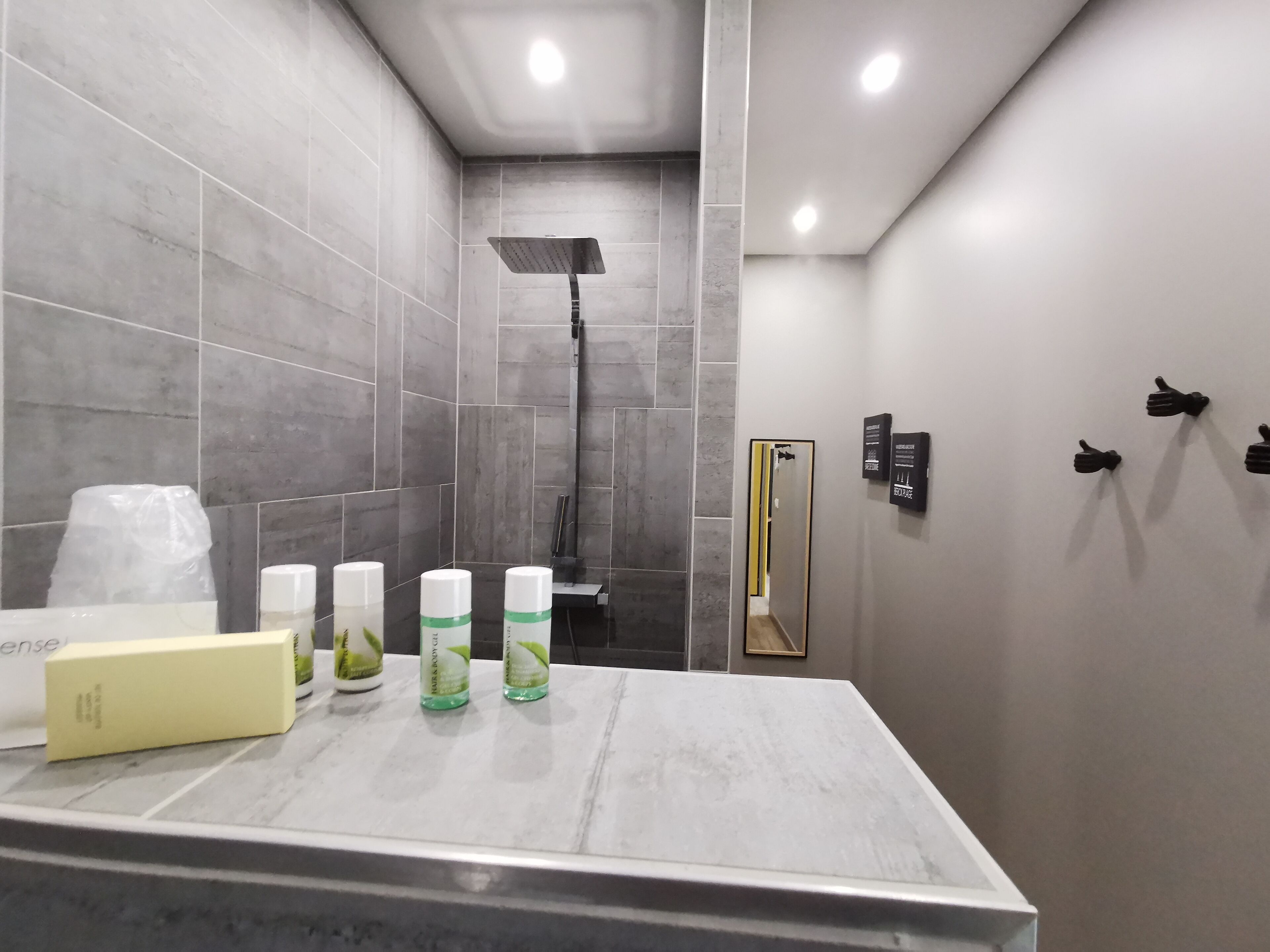 A modern bathroom with grey tiles, a shower, a vanity with toiletries, and a mirror with a gold frame.