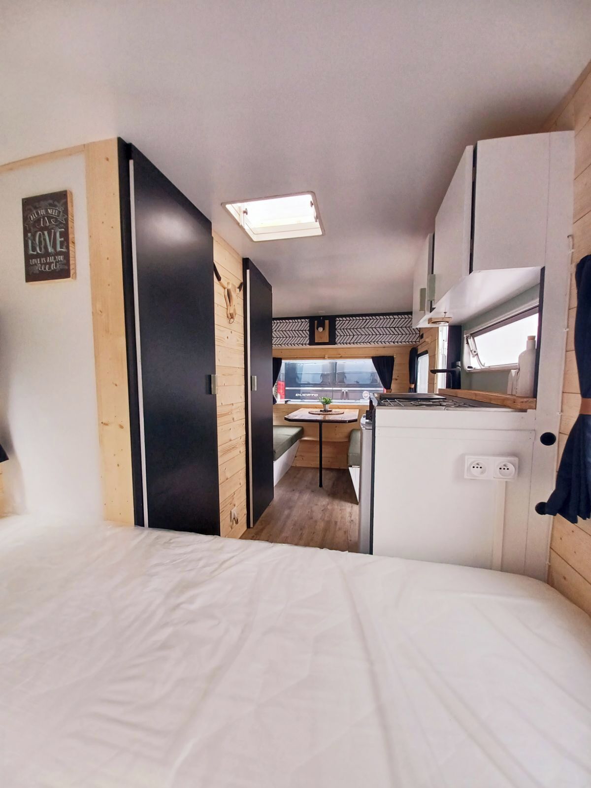 Ein kompaktes Wohnmobil-Interieur mit einer Küchenzeile, einer Essecke und einer Schlafgelegenheit.