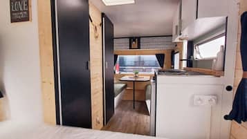 A compact RV interior with a kitchenette, a dining area, and a sleeping space.
