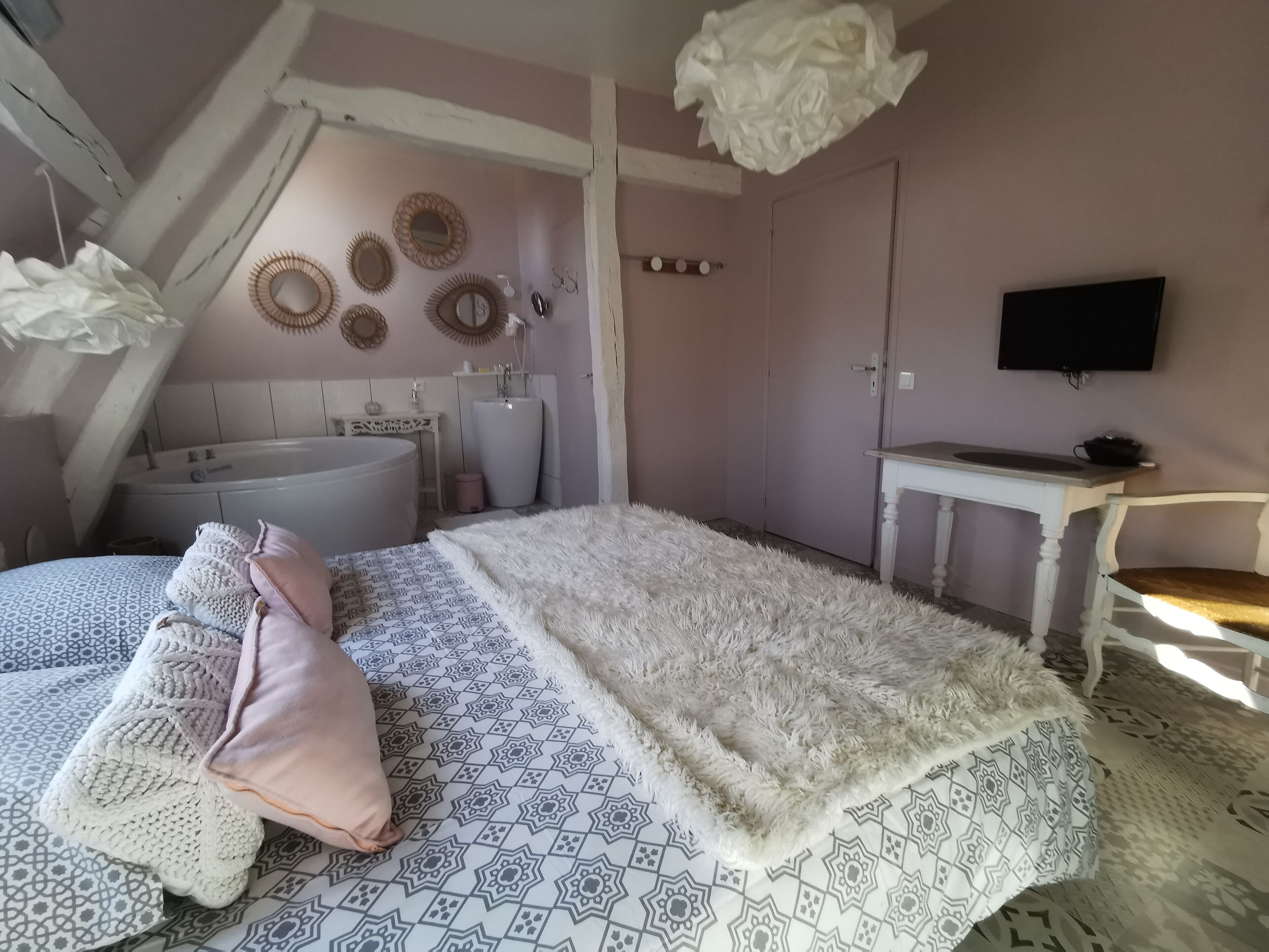 A bedroom with a large bed, a white fluffy throw, a patterned rug, a white dresser, a vanity with a mirror, and a ceiling fan.