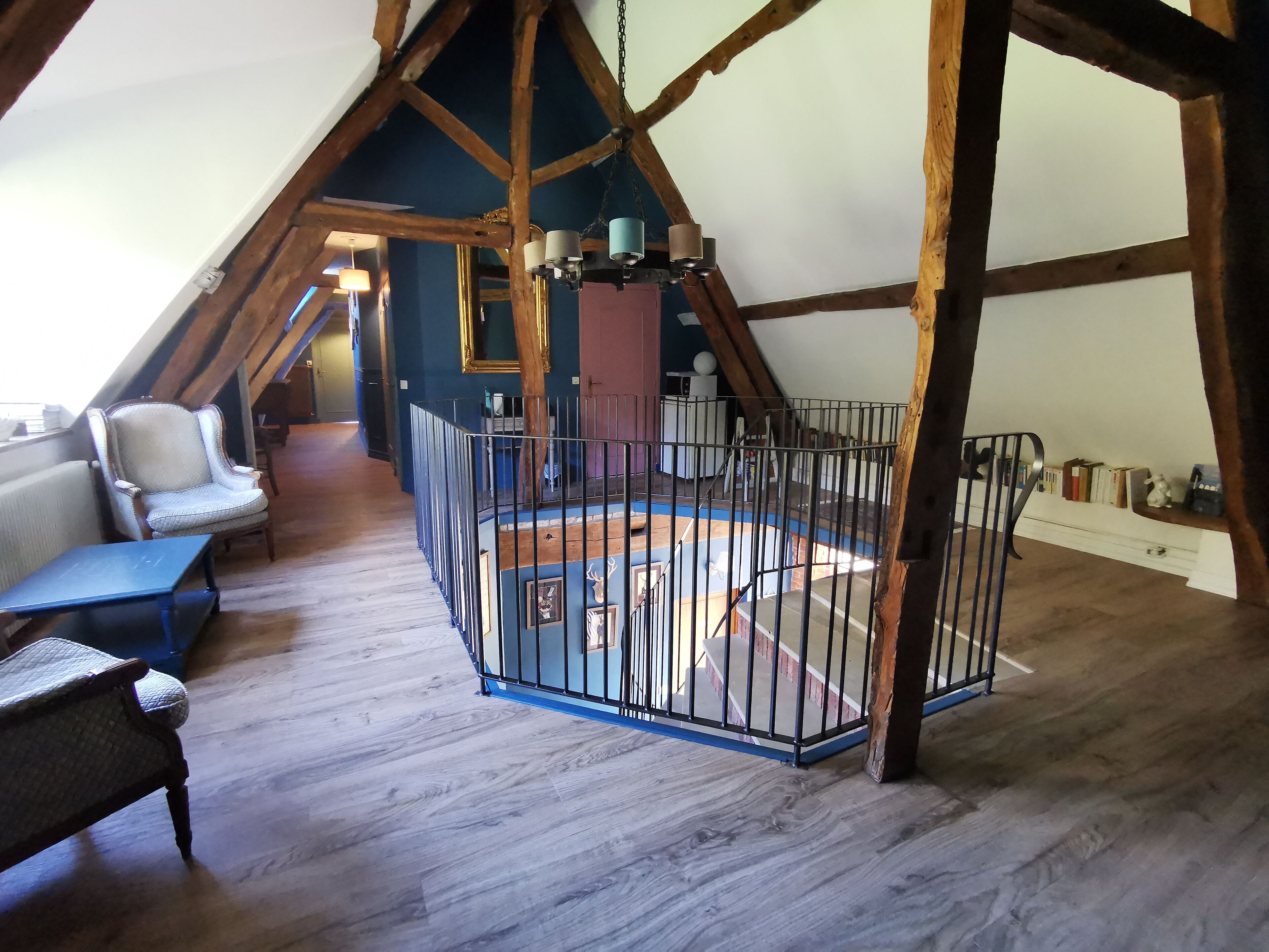A spacious attic room with exposed wooden beams, a blue play area, and a chair.
