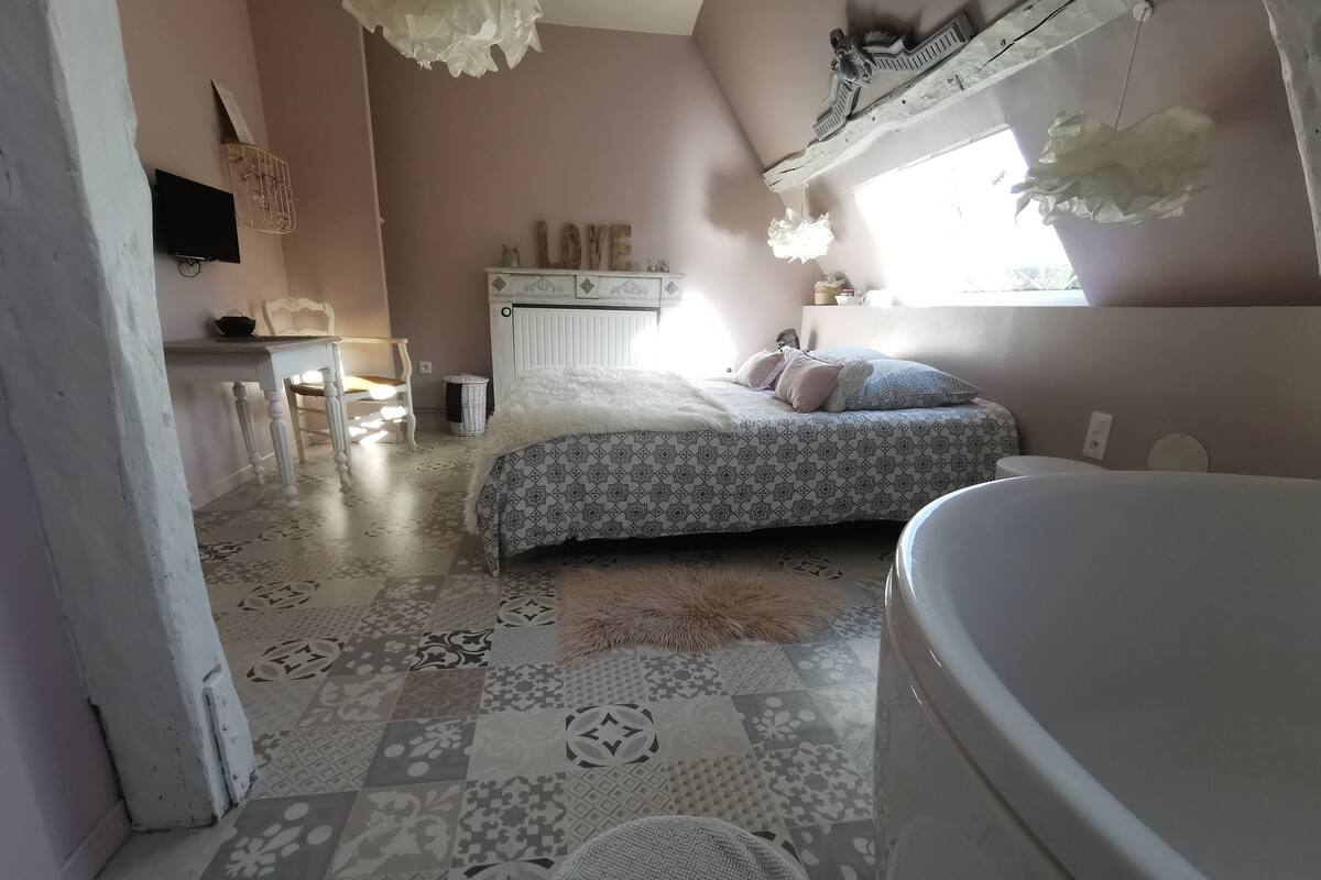 A bedroom with a patterned floor, a bed with a patterned bedspread, a white radiator, a small desk with a chair, and a window with a view of trees.