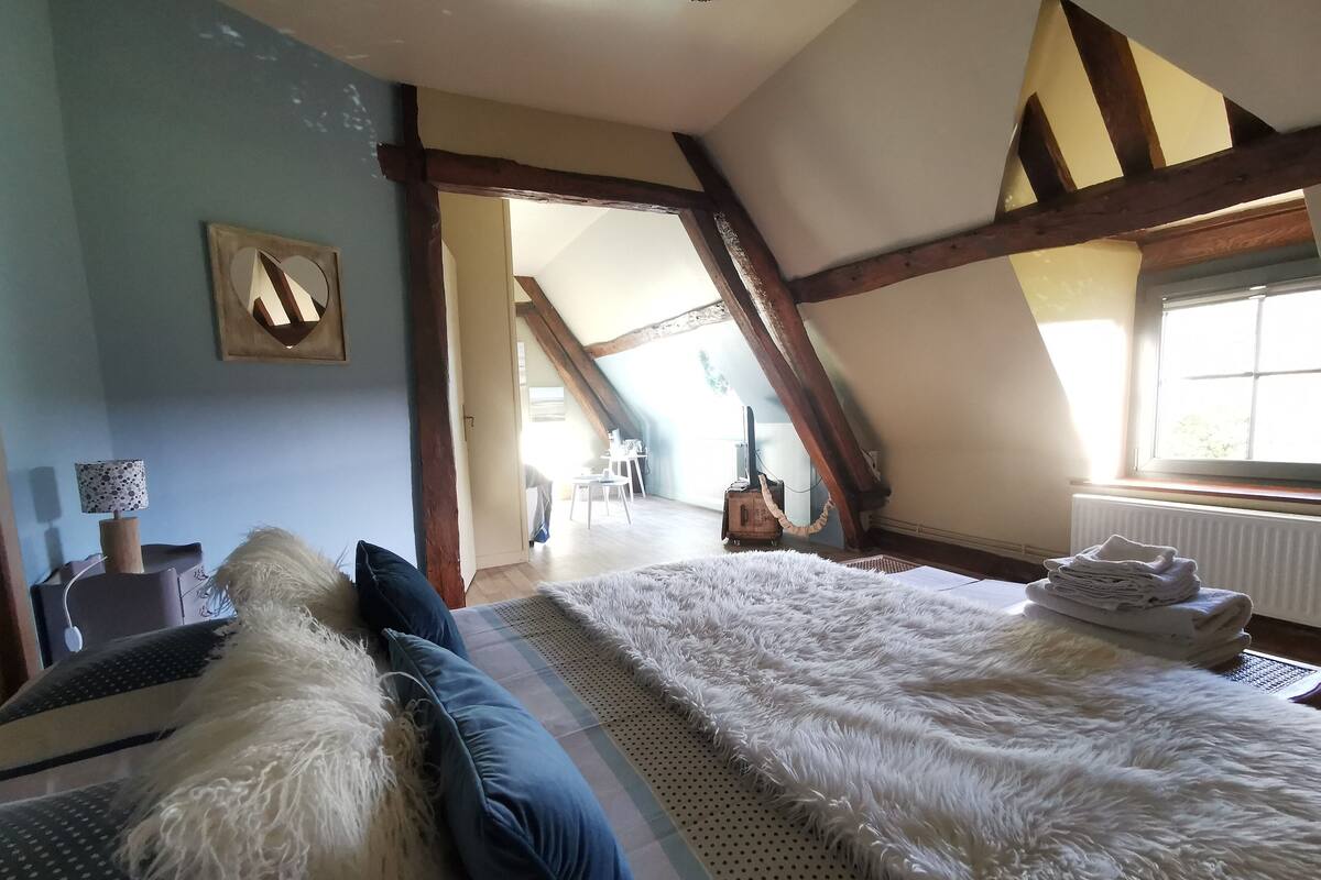A bedroom with a large bed, a wooden ceiling, and a view of a dining area.
