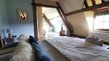 A bedroom with a large bed, a wooden ceiling, and a view of a dining area.