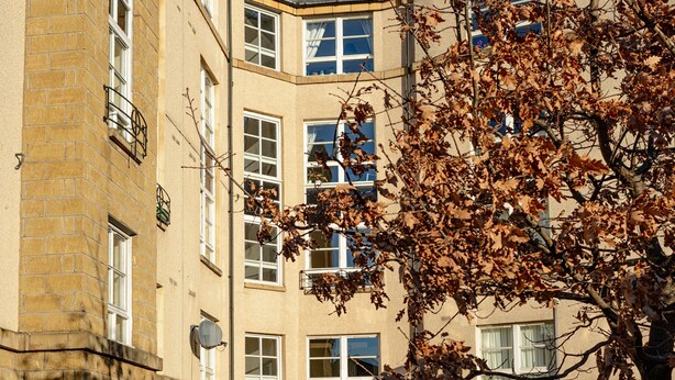 En flervåningsbyggnad med bostäder och en central innergård, med en stenlagd gångväg och en liten gräsyta.