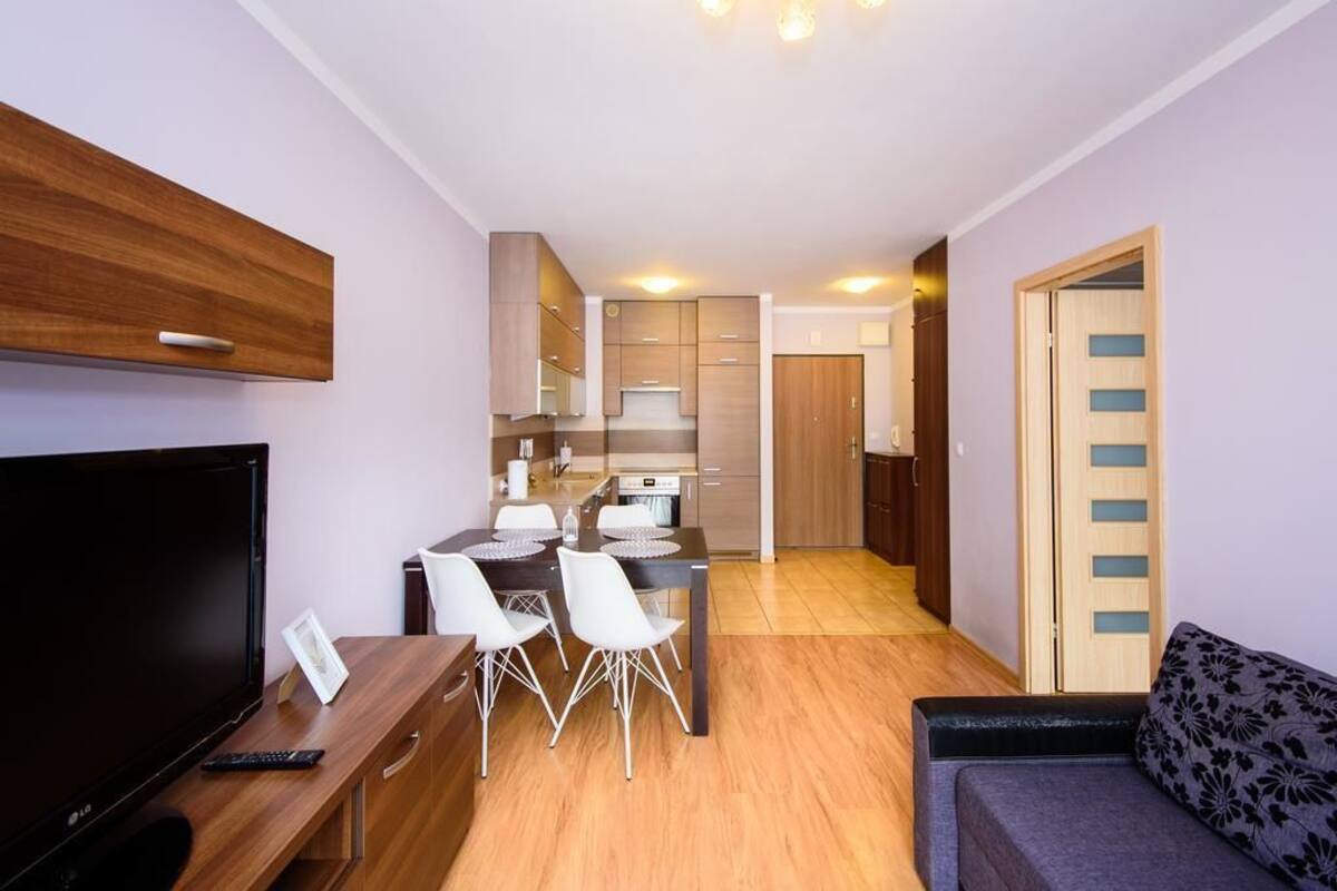 A modern living room with a flat-screen TV, wooden furniture, a dining area with a table and chairs, and a sofa.