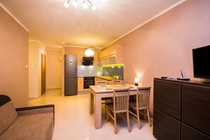 A compact living space with a kitchenette, a dining area with a table and chairs, and a dark-colored cabinet with a flat-screen TV. - Supreme Apartments Ściegiennego (Szczecin)