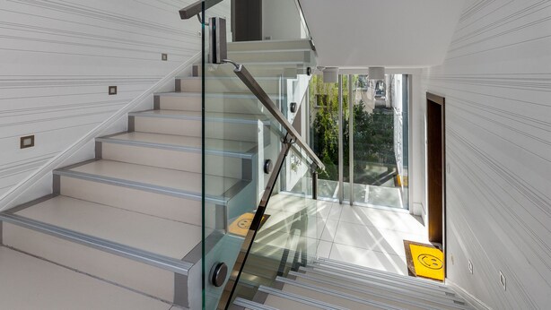 Un escalier moderne avec des rampes en verre et une vue sur la verdure environnante.