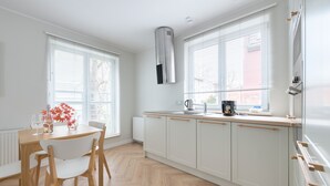 Une cuisine moderne avec des meubles blancs, une table à manger en bois et une fenêtre équipée de stores.