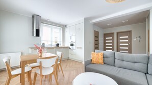 Un salon moderne avec un canapé gris, une table ronde blanche et un coin repas comprenant une table en bois et des chaises blanches.