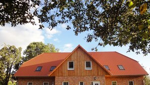 A two-story wooden house with a red-tiled roof, brick walls, and a small front porch. - Ostsee Ferienhaus Welzin - Schulgartenhaus (Damshagen)