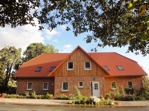 A two-story wooden house with a red-tiled roof, brick walls, and a small front porch.