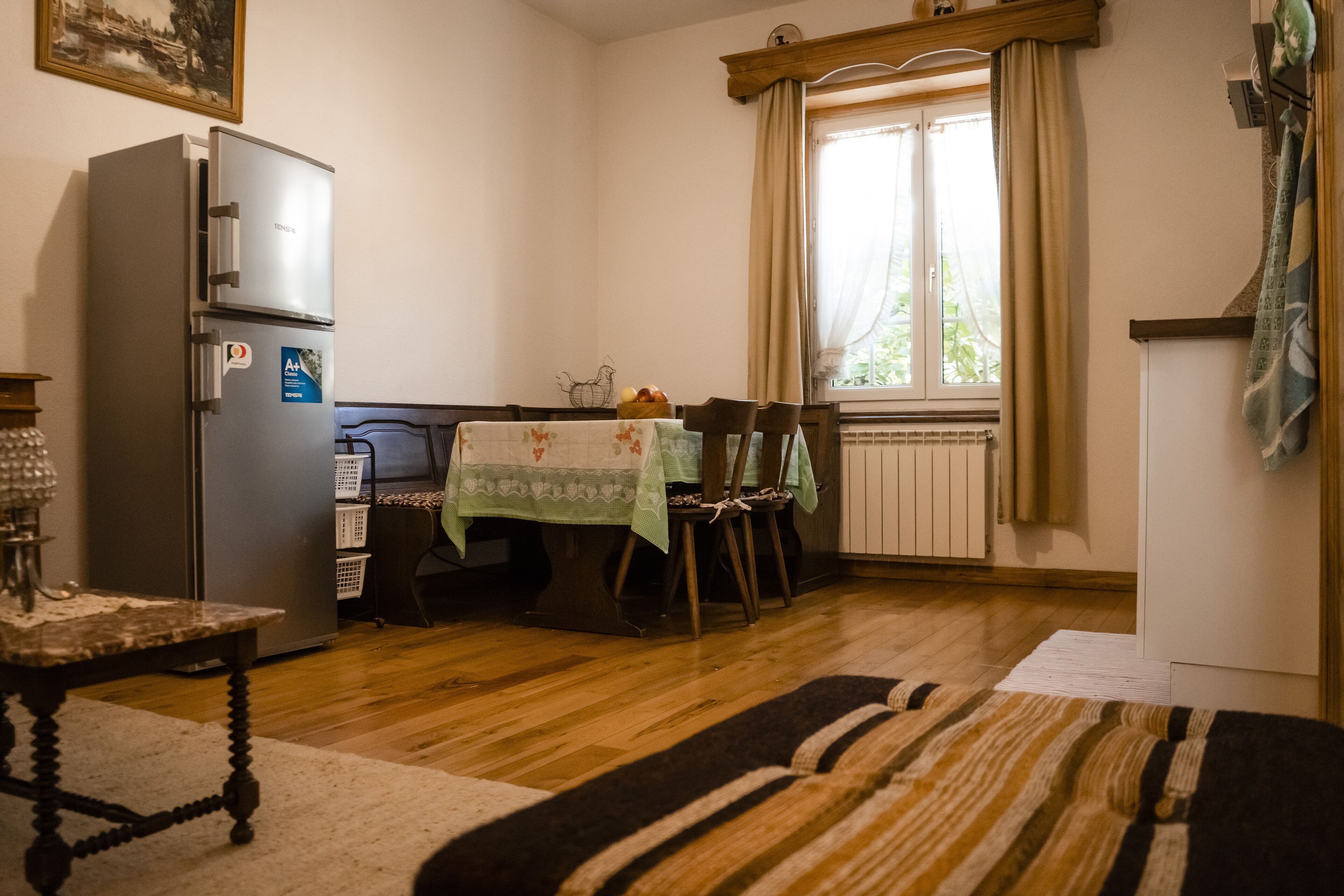 Eine kleine Küche mit Kühlschrank, Esstisch, Stühlen und einem Fenster mit Vorhängen.